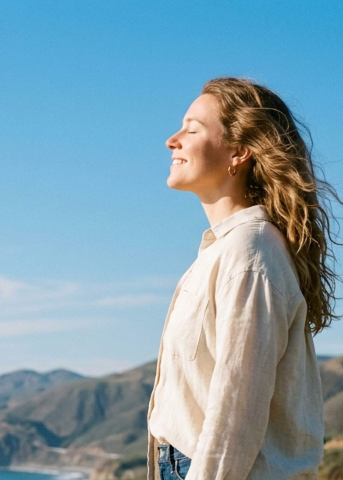 Woman standing outdoors in sunlight, eyes closed, looking calm and restored
